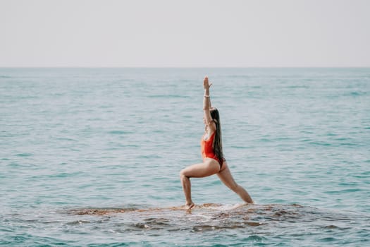 Woman sea yoga. Back view of free calm happy satisfied woman with long hair standing on top rock with yoga position against of sky by the sea. Healthy lifestyle outdoors in nature, fitness concept.