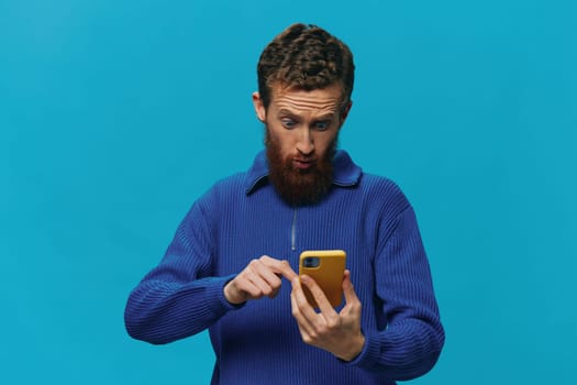 Portrait of a man with a phone in his hands does looking at it and talking on the phone, on a blue background. Communicating online social media, lifestyle. High quality photo