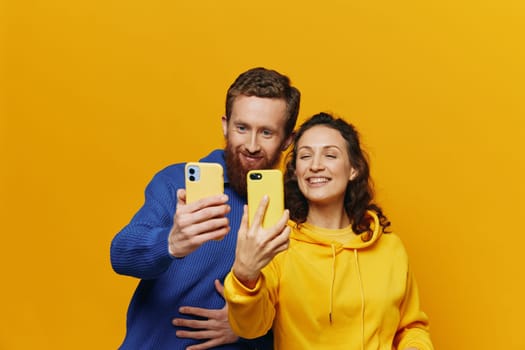 Man and woman couple smiling merrily with phone in hand social media viewing photos and videos, on yellow background, symbols signs and hand gestures, family freelancers. High quality photo