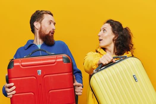 Woman and man smiling, suitcases in hand with yellow and red suitcase smiling merrily and crooked, yellow background, going on a trip, family vacation trip, newlyweds. High quality photo