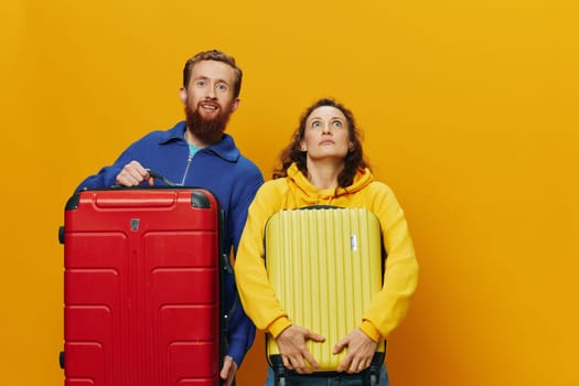 Woman and man smiling, suitcases in hand with yellow and red suitcase smiling merrily and crooked, yellow background, going on a trip, family vacation trip, newlyweds. High quality photo