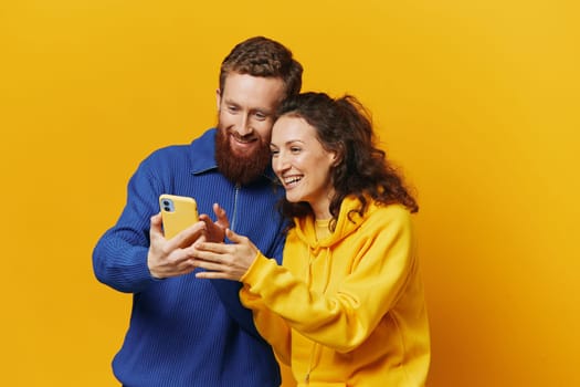 Man and woman couple smiling merrily with phone in hand social media viewing photos and videos, on yellow background, symbols signs and hand gestures, family freelancers. High quality photo