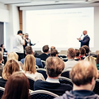 I have a question. Group of business people sitting at the chairs in conference hall. Businessman standing up asking a question. Conference and Presentation. Business and Entrepreneurship.