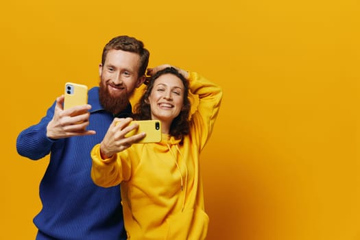 Man and woman couple smiling merrily with phone in hand social media viewing photos and videos, on yellow background, symbols signs and hand gestures, family freelancers. High quality photo