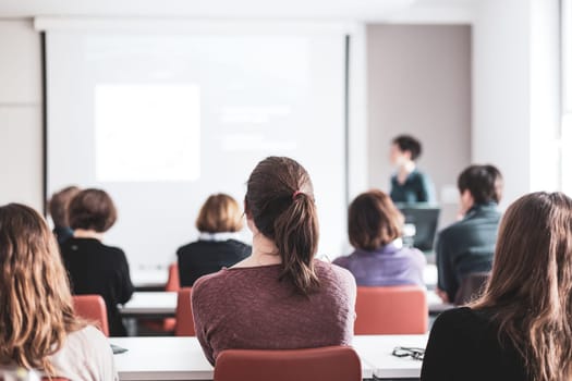 Female speaker giving presentation in lecture hall at university workshop . Participants listening to lecture and making notes. Scientific conference event.