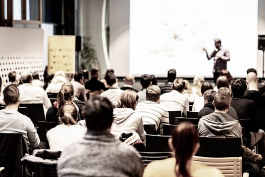 Speaker giving a talk in conference hall at business event. Audience at the conference hall. Business and Entrepreneurship concept. Focus on unrecognizable people in audience.