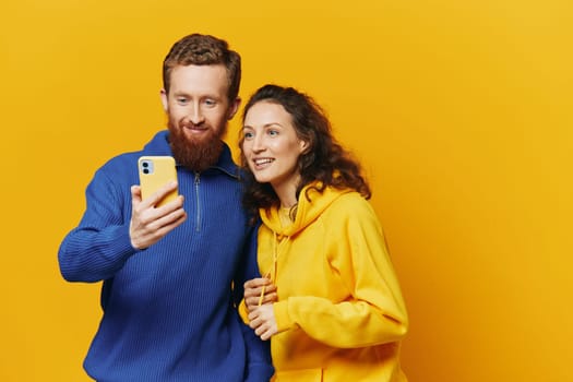 Man and woman couple smiling merrily with phone in hand social media viewing photos and videos, on yellow background, symbols signs and hand gestures, family freelancers. High quality photo