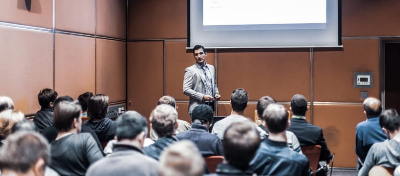 Speaker giving a talk in conference hall at business meeting event. Rear view of unrecognizable people in audience at the conference hall. Business and entrepreneurship concept.