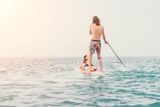 Sea woman and man on sup. Silhouette of happy young woman and man, surfing on SUP board, confident paddling through water surface. Idyllic sunset. Active lifestyle at sea or river