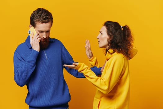 Man and woman couple with phone in hand call talking on the phone, on a yellow background, symbols signs and hand gestures, family quarrel jealousy and scandal. High quality photo