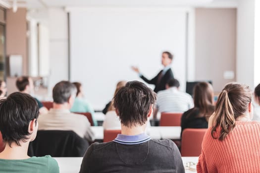 Speaker giving presentation in lecture hall at university. Participants listening to lecture and making notes. Copy space for brand on white screen.