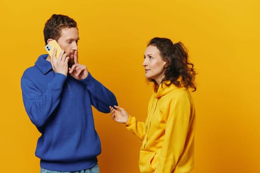 Man and woman couple with phone in hand call talking on the phone, on a yellow background, symbols signs and hand gestures, family quarrel jealousy and scandal. High quality photo