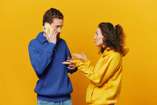 Man and woman couple with phone in hand call talking on the phone, on a yellow background, symbols signs and hand gestures, family quarrel jealousy and scandal. High quality photo