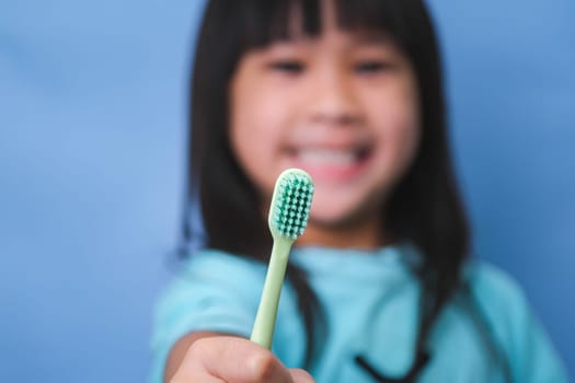 Smiling cute little girl holding toothbrush isolated on blue background. Cute little child brushing teeth. Kid training oral hygiene, Tooth decay prevention or dental care concept.