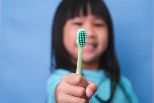 Smiling cute little girl holding toothbrush isolated on blue background. Cute little child brushing teeth. Kid training oral hygiene, Tooth decay prevention or dental care concept.