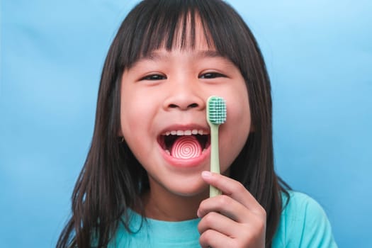 Smiling cute little girl holding toothbrush isolated on blue background. Cute little child brushing teeth. Kid training oral hygiene, Tooth decay prevention or dental care concept.