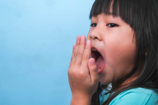 Little asian girl covering her mouth to smell the bad breath. Child girl checking breath with her hands. Oral health problems or dental care concept.