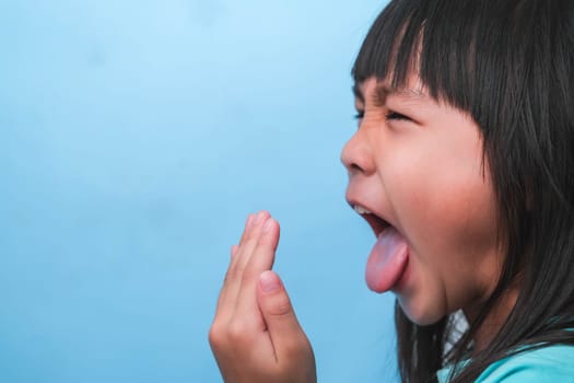 Little asian girl covering her mouth to smell the bad breath. Child girl checking breath with her hands. Oral health problems or dental care concept.