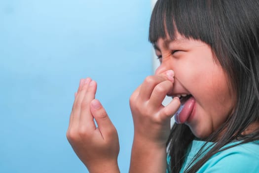 Little asian girl covering her mouth to smell the bad breath. Child girl checking breath with her hands. Oral health problems or dental care concept.