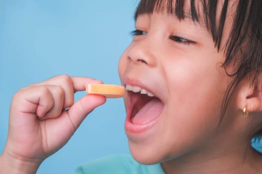 Smiling cute little girl eating sweet gelatin with sugar added isolated on blue background. Children eat sugary sweets, causing loss teeth or tooth decay and unhealthy oral care.