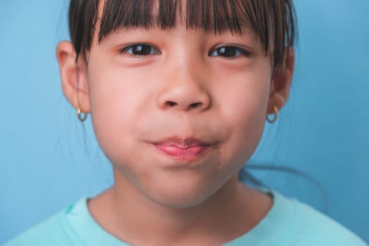 Smiling cute little girl eating sweet gelatin with sugar added isolated on blue background. Children eat sugary sweets, causing loss teeth or tooth decay and unhealthy oral care.