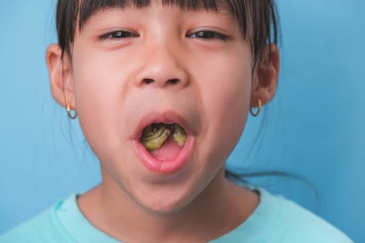 Smiling cute little girl eating sweet gelatin with sugar added isolated on blue background. Children eat sugary sweets, causing loss teeth or tooth decay and unhealthy oral care.