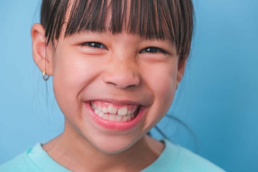 Close-up of smiling young girl revealing her beautiful white teeth on a blue background. Concept of good health in childhood.