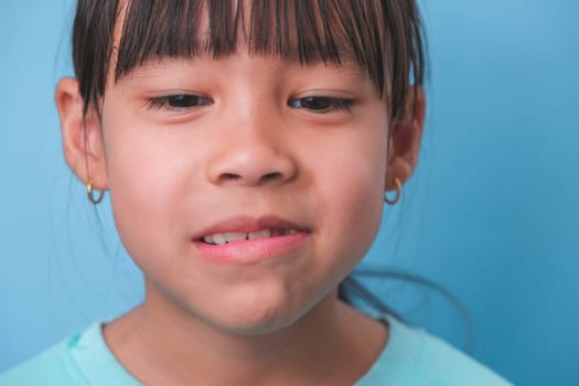 Smiling cute little girl eating sweet gelatin with sugar added isolated on blue background. Children eat sugary sweets, causing loss teeth or tooth decay and unhealthy oral care.