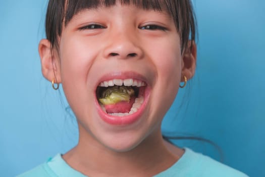 Smiling cute little girl eating sweet gelatin with sugar added isolated on blue background. Children eat sugary sweets, causing loss teeth or tooth decay and unhealthy oral care.