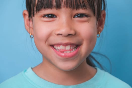 Close-up of smiling young girl revealing her beautiful white teeth on a blue background. Concept of good health in childhood.