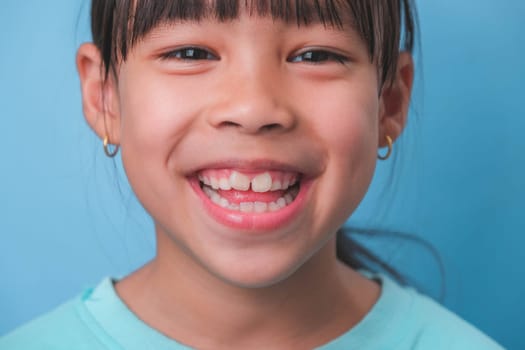 Close-up of smiling young girl revealing her beautiful white teeth on a blue background. Concept of good health in childhood.