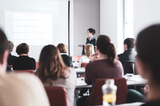 Female speaker giving presentation in lecture hall at university workshop . Participants listening to lecture and making notes. Scientific conference event.