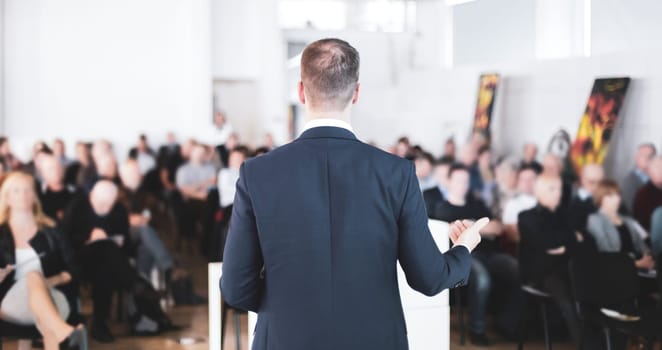 Speaker at Business Conference with Public Presentations. Audience at the conference hall. Entrepreneurship club. Rear view. Horisontal composition. Background blur.