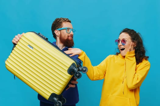 Woman and man smile sitting on suitcase with yellow suitcase smile, on blue background, packing for trip, family vacation trip. High quality photo