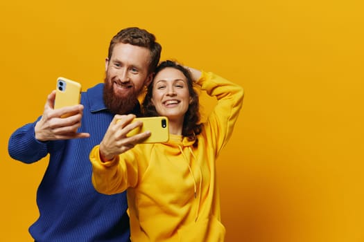 Man and woman couple smiling merrily with phone in hand social media viewing photos and videos, on yellow background, symbols signs and hand gestures, family freelancers. High quality photo