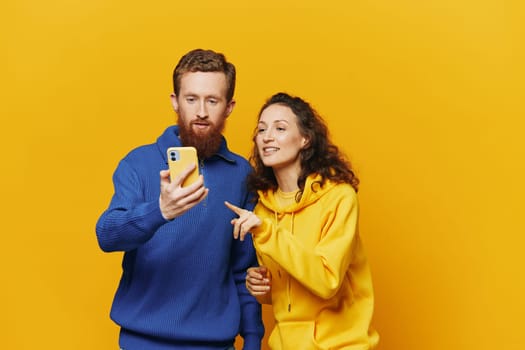 Man and woman couple with phone in hand call talking on the phone, on a yellow background, symbols signs and hand gestures, family quarrel jealousy and scandal. High quality photo