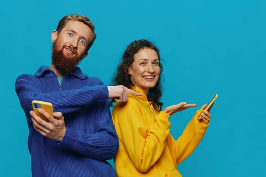 Woman and man cheerful couple with phones in their hands crooked smile cheerful, on blue background. The concept of real family relationships, talking on the phone, work online. High quality photo