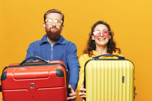 Woman and man smiling, suitcases in hand with yellow and red suitcase smiling merrily and crooked, yellow background, going on a trip, family vacation trip, newlyweds. High quality photo