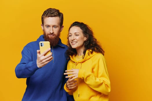 Man and woman couple smiling merrily with phone in hand social media viewing photos and videos, on yellow background, symbols signs and hand gestures, family freelancers. High quality photo