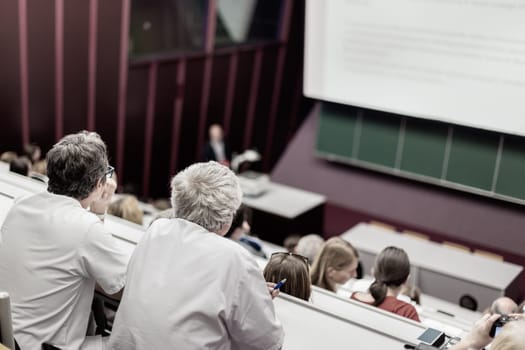 Lecturer at university. Healthcare expert giving a talk to medical faculty professors. Participants listening to lecture and making notes.