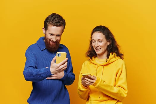 Man and woman couple smiling merrily with phone in hand social media viewing photos and videos, on yellow background, symbols signs and hand gestures, family freelancers. High quality photo