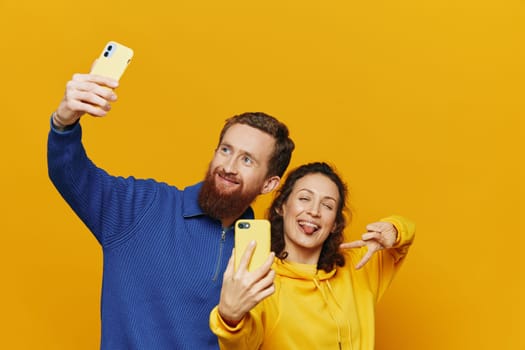 Man and woman couple smiling merrily with phone in hand social media viewing photos and videos, on yellow background, symbols signs and hand gestures, family freelancers. High quality photo