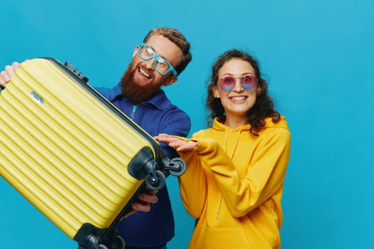 Woman and man smile sitting on suitcase with yellow suitcase smile, on blue background, packing for trip, family vacation trip. High quality photo