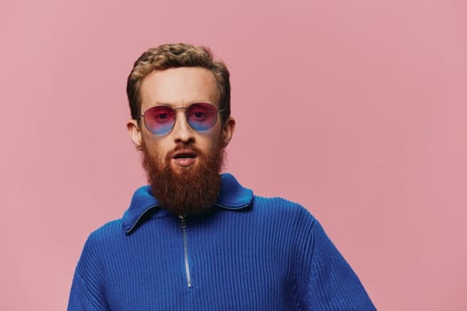 Portrait of a redheaded man wearing sunglasses smiling and dancing, listening to music on a pink background. Hipster with a beard, happiness finger pointing. High quality photo