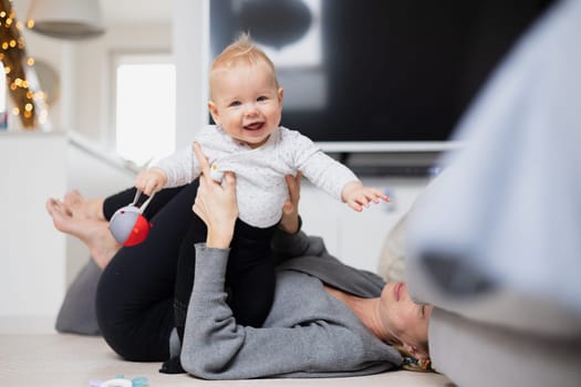 Happy family moments. Mother lying comfortably on children's mat playing with her baby boy watching and suppervising his first steps. Positive human emotions, feelings, joy