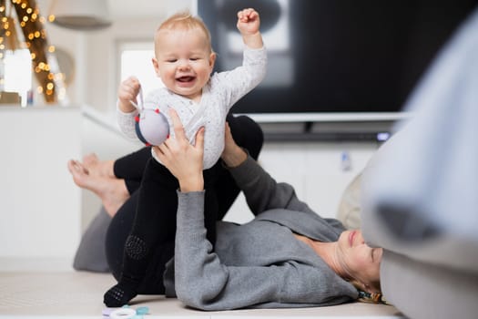 Happy family moments. Mother lying comfortably on children's mat playing with her baby boy watching and suppervising his first steps. Positive human emotions, feelings, joy