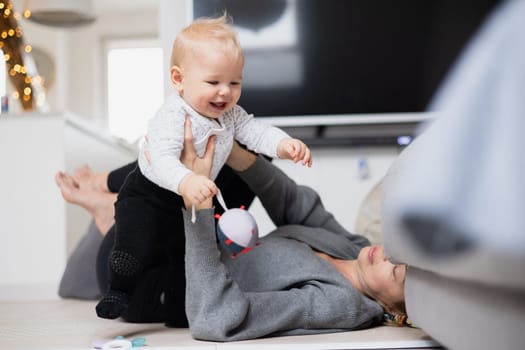 Happy family moments. Mother lying comfortably on children's mat playing with her baby boy watching and suppervising his first steps. Positive human emotions, feelings, joy