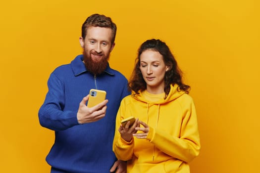 Man and woman couple smiling merrily with phone in hand social media viewing photos and videos, on yellow background, symbols signs and hand gestures, family freelancers. High quality photo