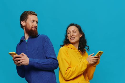 Woman and man cheerful couple with phones in their hands crooked smile cheerful, on blue background. The concept of real family relationships, talking on the phone, work online. High quality photo