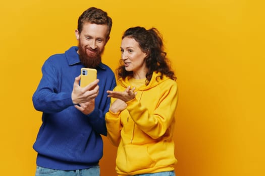 Man and woman couple smiling merrily with phone in hand social media viewing photos and videos, on yellow background, symbols signs and hand gestures, family freelancers. High quality photo